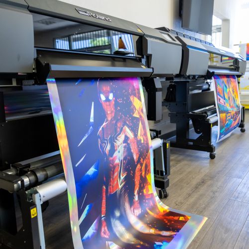 Large-format printer with colorful output displaying a superhero design.